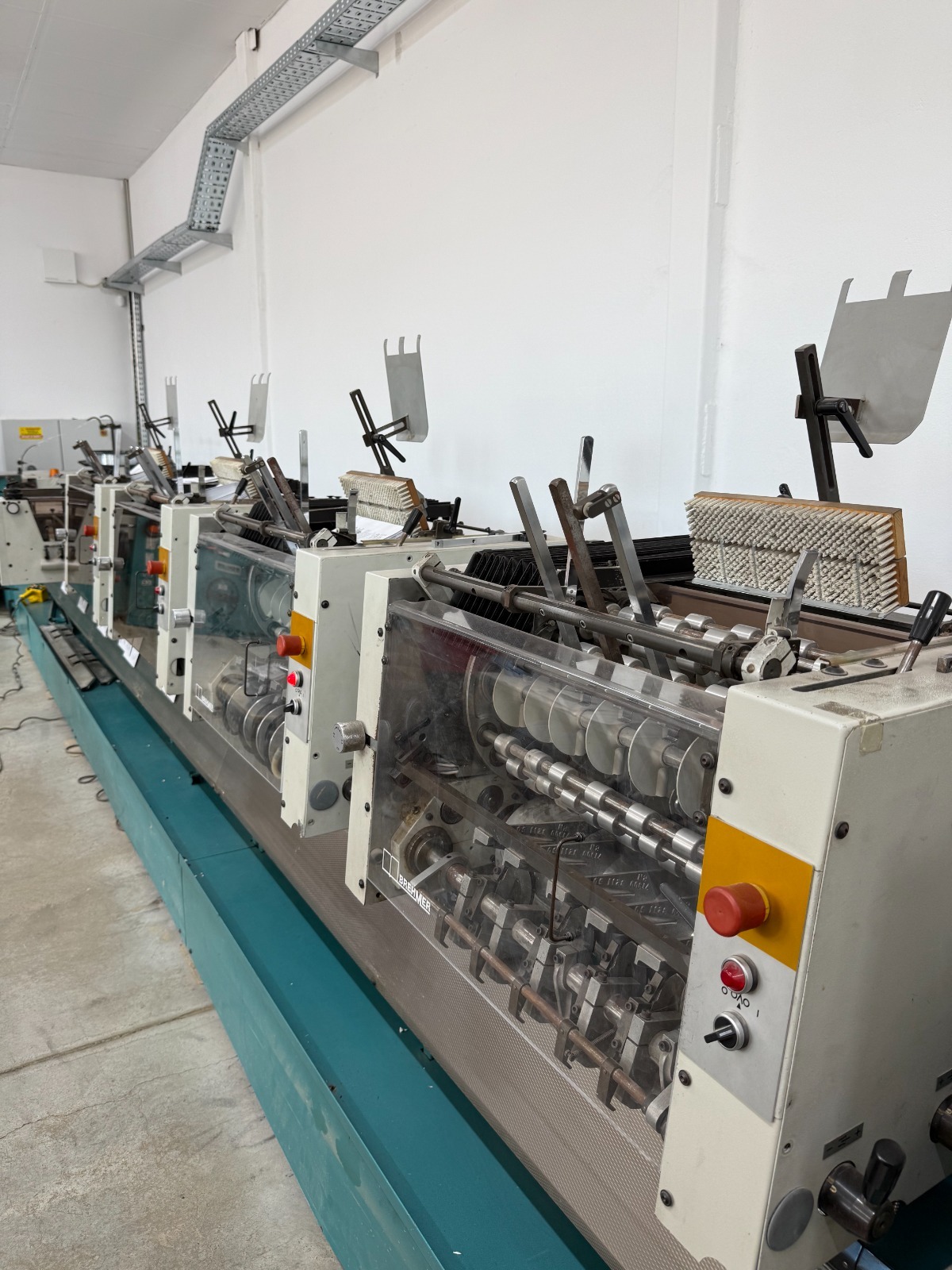 Used BREHMER McCAIN S 1000 C / TR 100 – Industrial Saddle Stitching Line, 6 Automatic Feeders + 1 Manual Feeding Station, Hohner Stitching Head, Integrated Three-Knife Trimmer Configuration to Be Confirmed, Professional Booklet Production