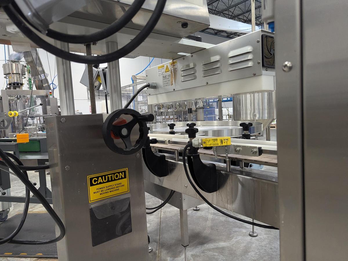 Used Aesus 6-Head Filling Line with Descrambler. Labeler, Filler, Capper, Induction Sealer & Accumulation Table