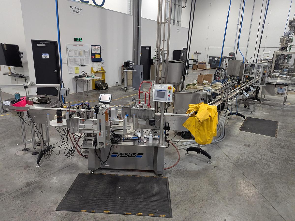 Used Aesus 6-Head Filling Line with Descrambler. Labeler, Filler, Capper, Induction Sealer & Accumulation Table