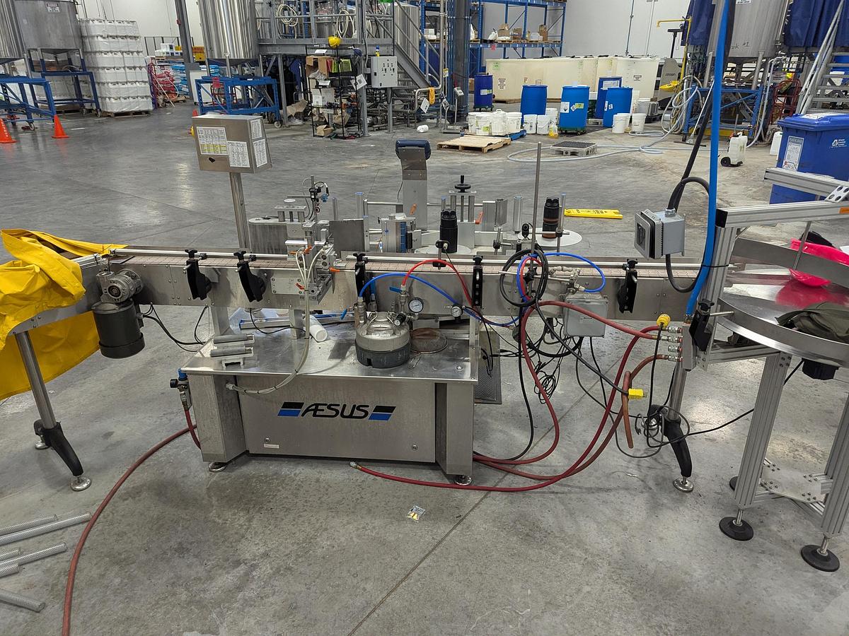 Used Aesus 6-Head Filling Line with Descrambler. Labeler, Filler, Capper, Induction Sealer & Accumulation Table