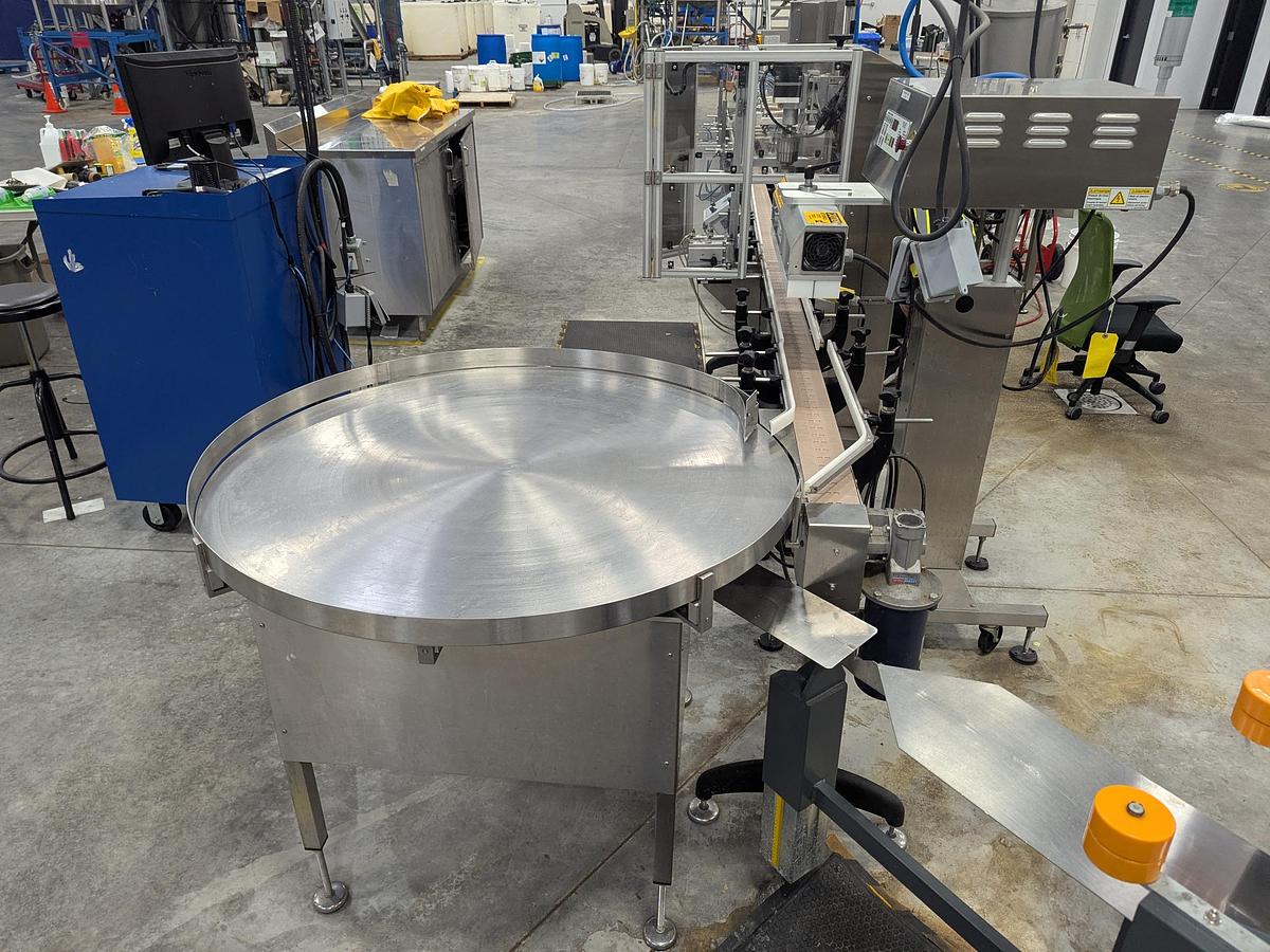 Used Aesus 6-Head Filling Line with Descrambler. Labeler, Filler, Capper, Induction Sealer & Accumulation Table