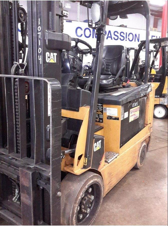 Front angled view of refurbished 2012 Cat E6000 4‑wheel electric forklift showing load backrest, solid tires, 48 volt chassis, 3‑stage mast with side shift, and CSA certification decal during Brampton deployment.