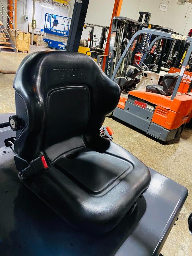 Close-up view of newly installed replacement seat on electric forklift showing cushion contour, seatbelt mount, and CSA safety decal during Brampton deployment