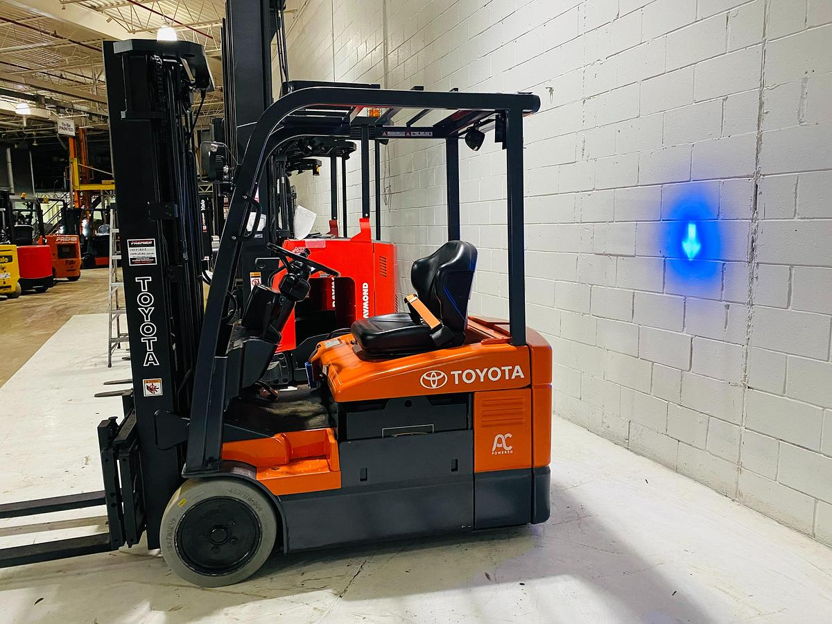 Opposite side view of 2012 Toyota 7FBEU15 electric forklift showing mast rails, CSA decals, and chassis profile during Brampton deployment