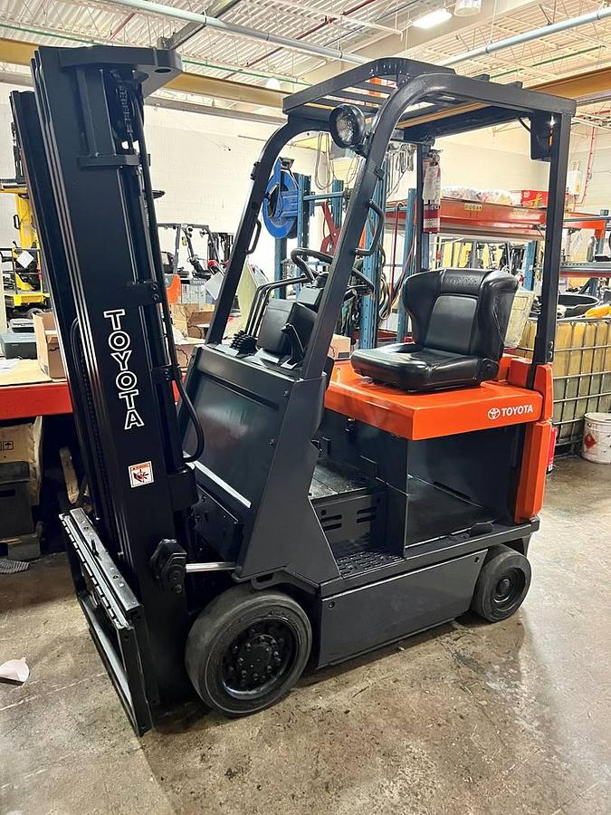 Side view of refurbished 2005 Toyota 7FBCU15 electric 4-wheel sit-down forklift showing triple mast, CSA decal, and 42" forks during Ontario deployment