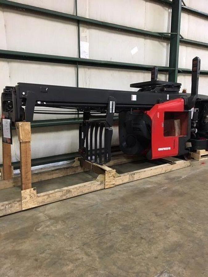 Side view of refurbished Raymond 750DR32TT deep-reach forklift laid down and cradled on flatbed trailer for delivery, showing triple mast secured with straps and chassis blocked for transport during Brampton deployment