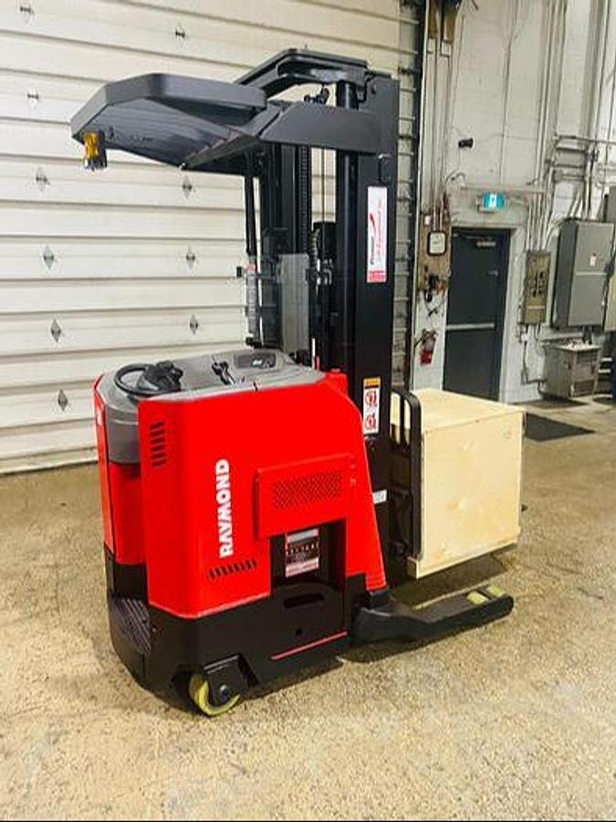 Rear side view of refurbished 2014 Raymond 750-R45TT EE-rated reach truck showing new charger staged in box on forks during Ontario deployment