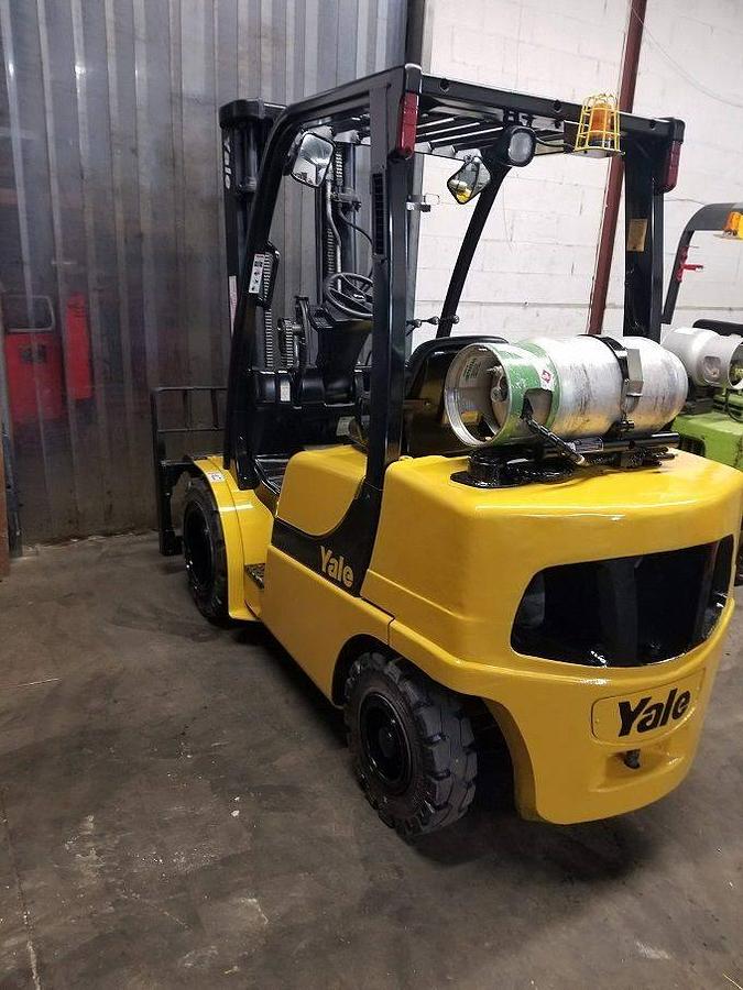 Rear side view of refurbished 2013 Yale GLP060VX LPG pneumatic forklift showing counterweight, propane tank mount, side shift carriage, and new treaded solid pneumatic tires during Brampton deployment