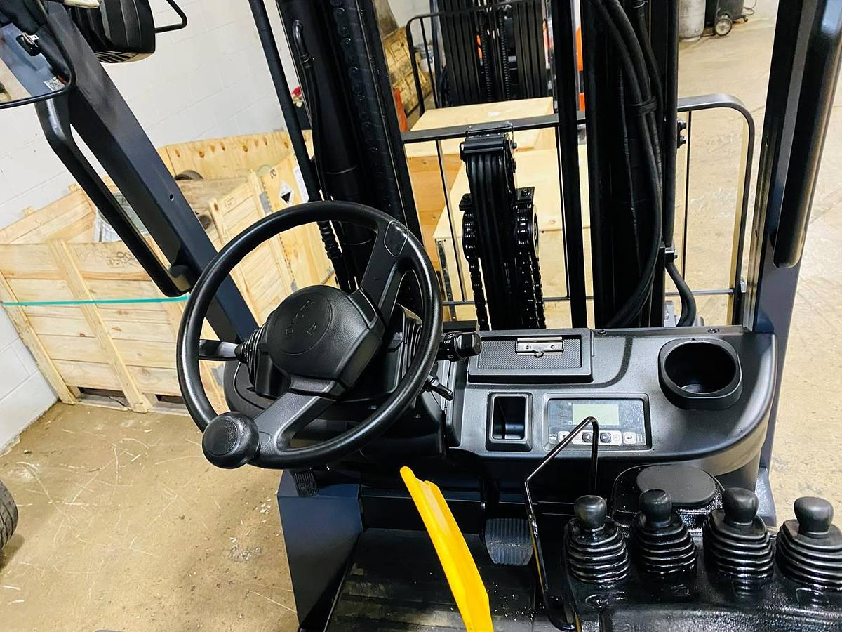 Operator compartment view of electric forklift showing steering wheel, instrument cluster, and CSA safety decals during Brampton deployment