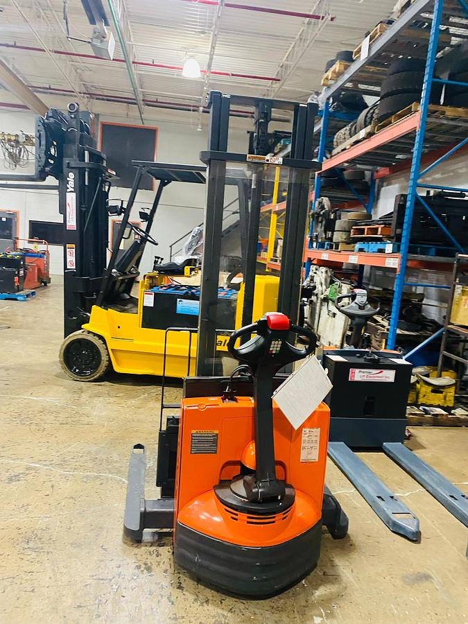Back view of refurbished 2014 Toyota 7BWS10 electric walkie straddle stacker showing operator handle, rear wheels, and CSA certification decal during Ontario deployment