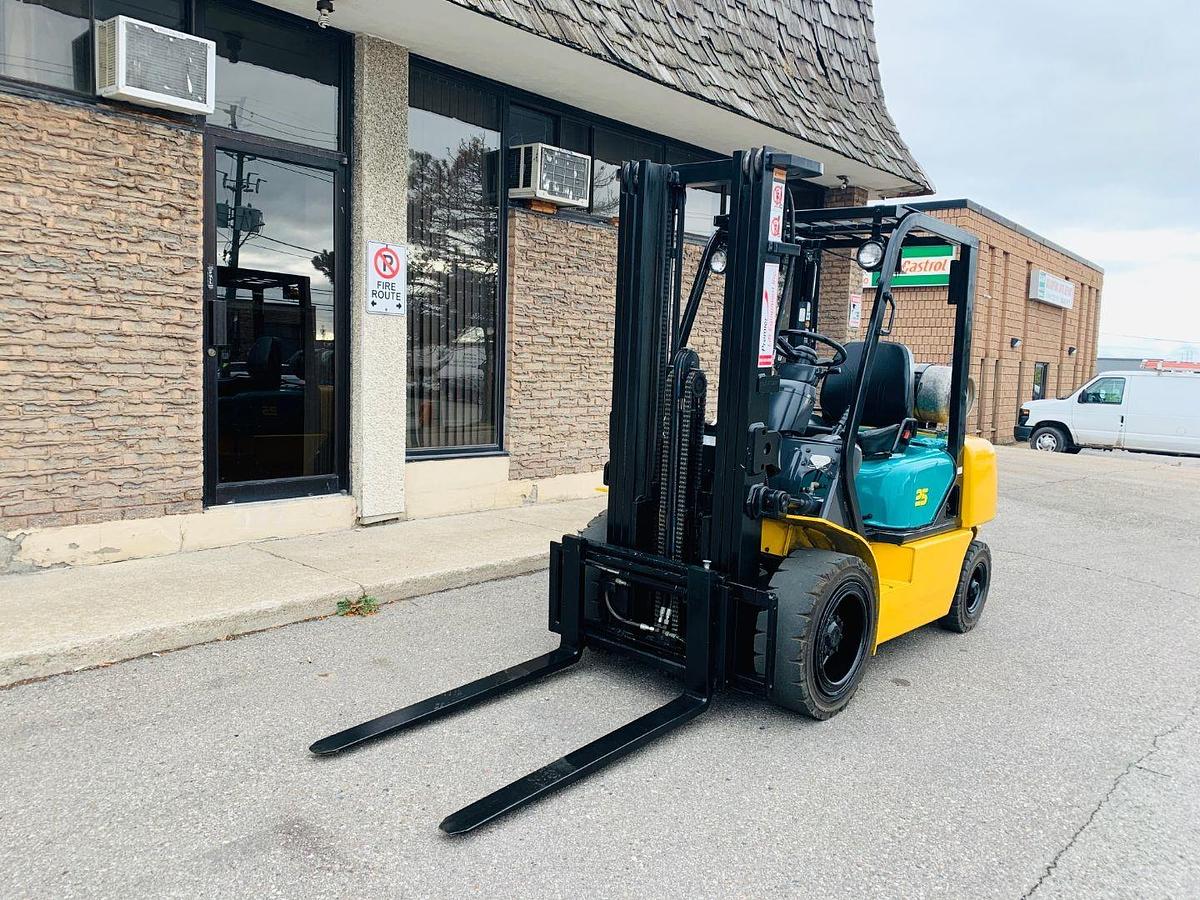 Front side view of refurbished 2008 Komatsu FG25T‑14 pneumatic tire forklift showing 5,000 lb capacity, LP gas tank, three‑stage mast, and CSA certification decal during Brampton deployment.