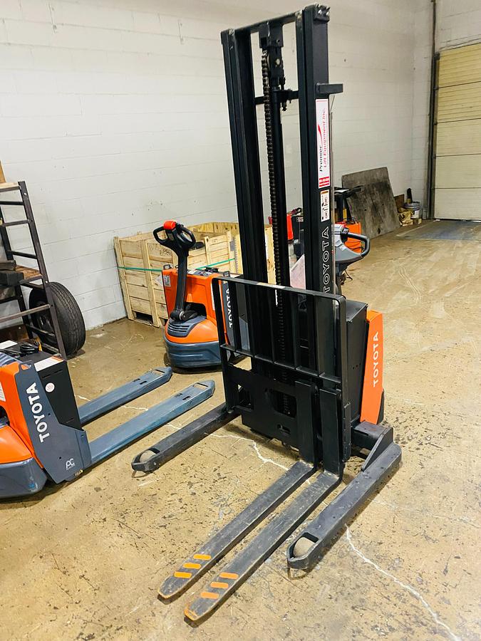 Front angle side view of refurbished 2014 Toyota 7BWS10 electric walkie straddle stacker showing fork tips, mast rails, and CSA certification decal during Ontario deployment