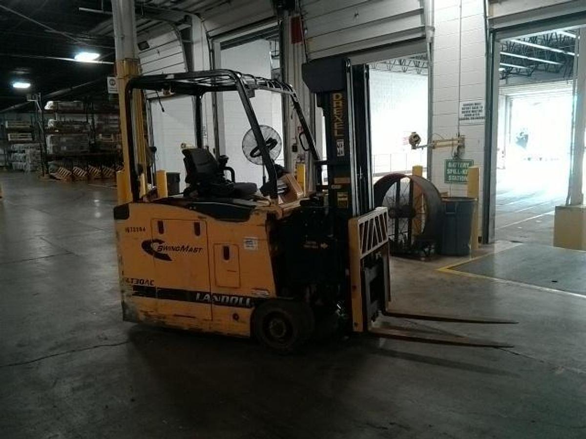 Side profile of Drexel SLT30AC 3-wheel SwingMast forklift showing triple mast, pivoting carriage, directional wheels, and narrow chassis during Brampton deployment