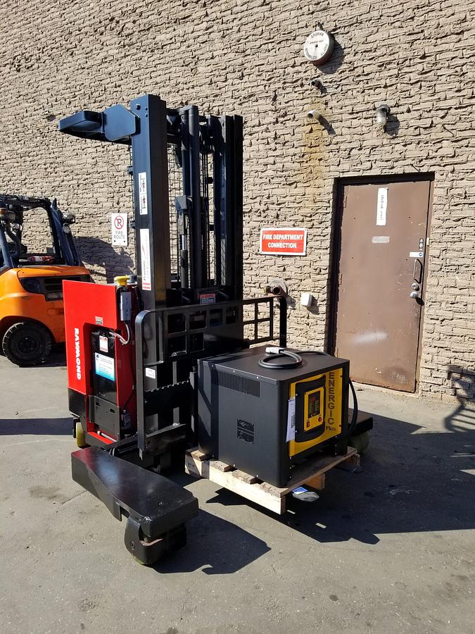 Front angled view showing mast rails and 42” fork tips with compatible charger on pallet