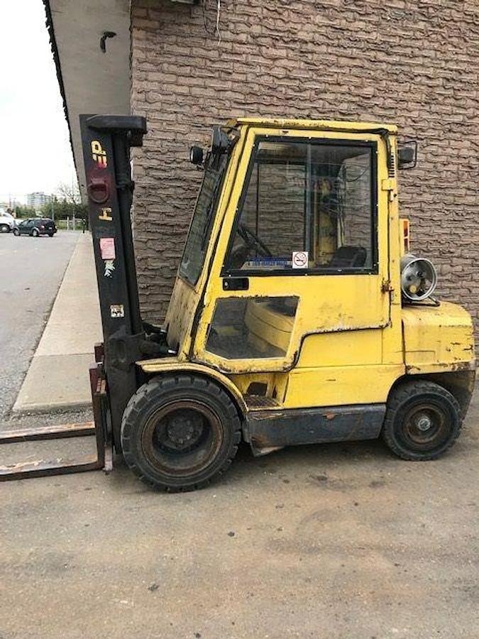 Side view of refurbished 2000 Hyster H60XM LP Gas forklift showing full cab, solid pneumatic tires, and 3‑stage mast without side shift during Erin, Ontario deployment.
