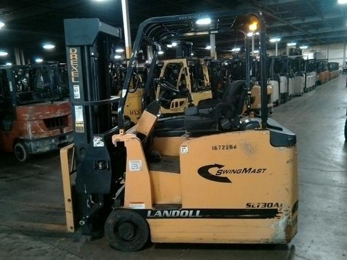 Side profile of Drexel SLT30AC 3-wheel SwingMast forklift showing triple mast, pivoting carriage, directional wheels, and narrow chassis during Brampton deployment