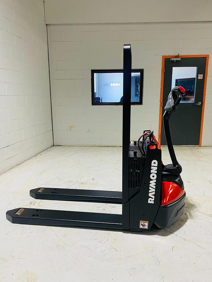 Opposite side view of 2018 Raymond 8210 electric walkie pallet jack shown chassis only without battery or charger – CSA-certified 4,500 lb unit featuring 27” x 45” tapered forks, 24V electric powertrain, thumb throttle controls, and non-marking polyurethane tires staged in Brampton ON; battery and charger available separately as extra options new or used – Premier Lift Equipment