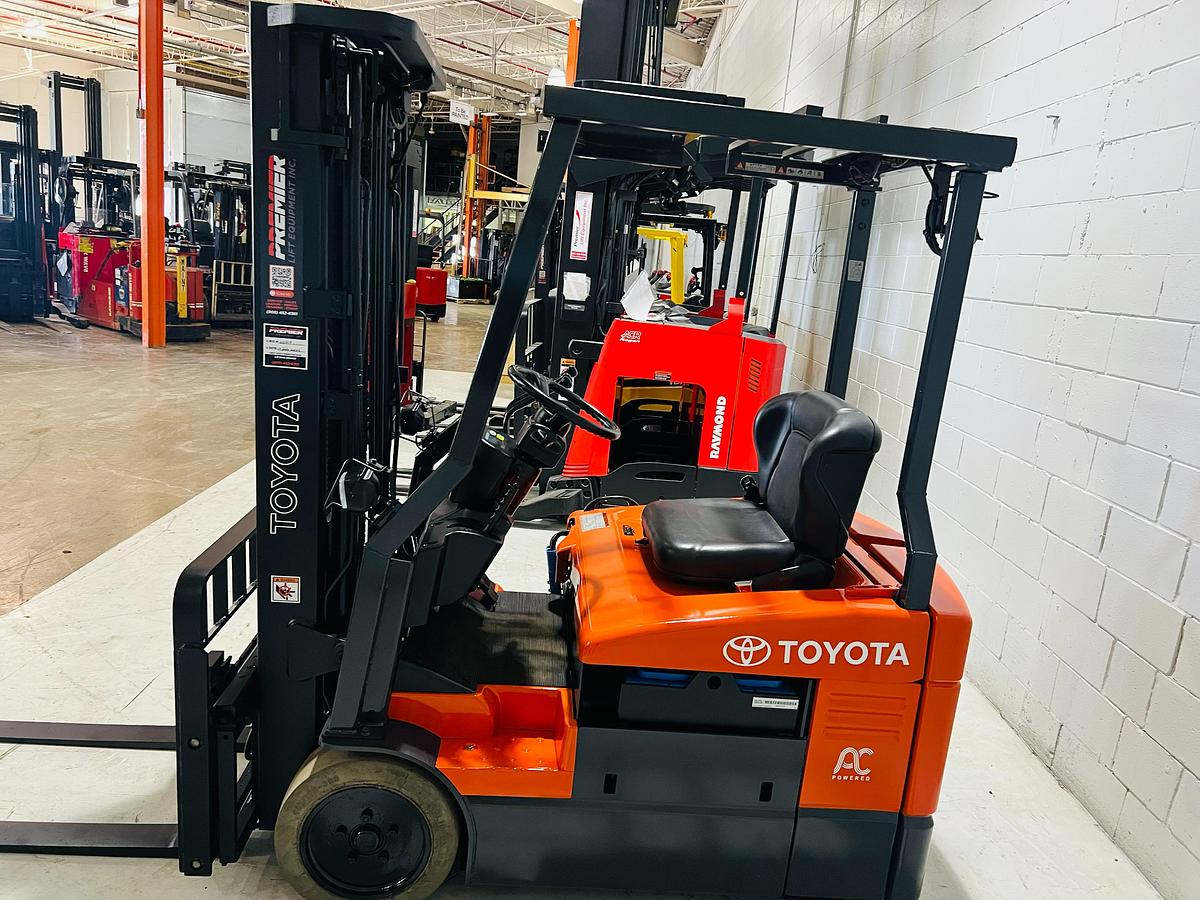 Opposite side view of 2014 Toyota 7FBEU15 electric forklift showing trimmed overhead guard, CSA decals, and 3-wheel chassis during Brampton deployment