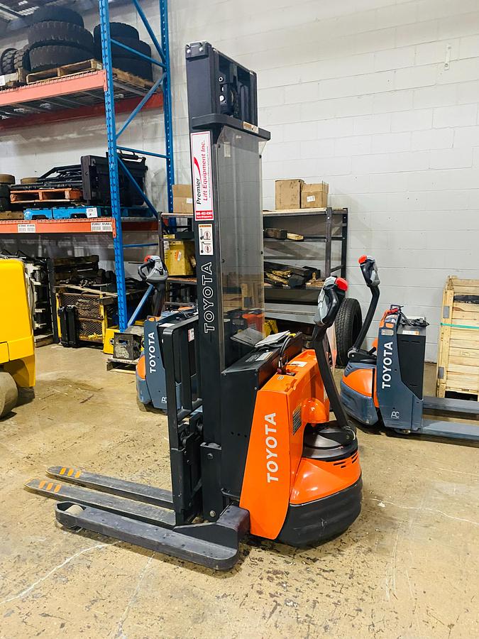 Side view of refurbished 2014 Toyota 7BWS10 electric walkie straddle stacker showing mast rails, CSA decal, and adjustable straddle legs during Ontario deployment