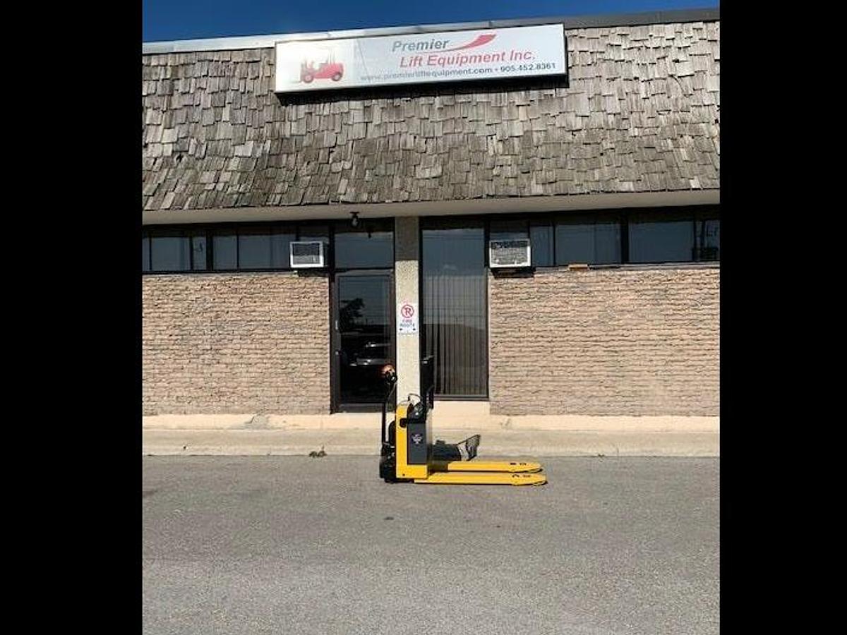 Side view of refurbished 2010 Yale MPB040 electric walkie pallet jack showing 27" x 48" forks, CSA decal, and vintage Premier Lift Equipment sign in background during Ontario deployment