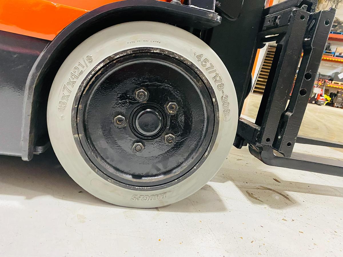Close-up of non-marking right side drive wheel on Toyota 7FBEU15 electric forklift with CSA decal and triple mast profile visible