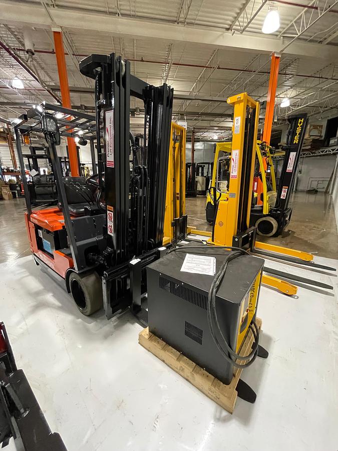 Front angled view showing mast rails,compact chassis profile with charger on forks