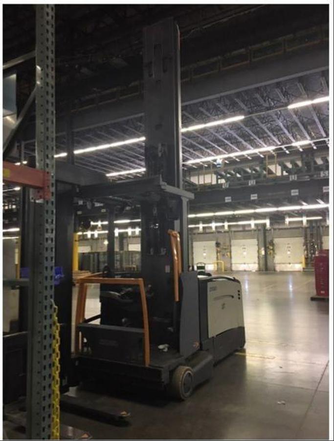Opposite front side angled view of refurbished 2017 Crown TSP7000 electric turret truck showing turret mast, wire guidance system, 72 volt battery compartment, operator cab, and CSA certification decal during Ontario deployment.