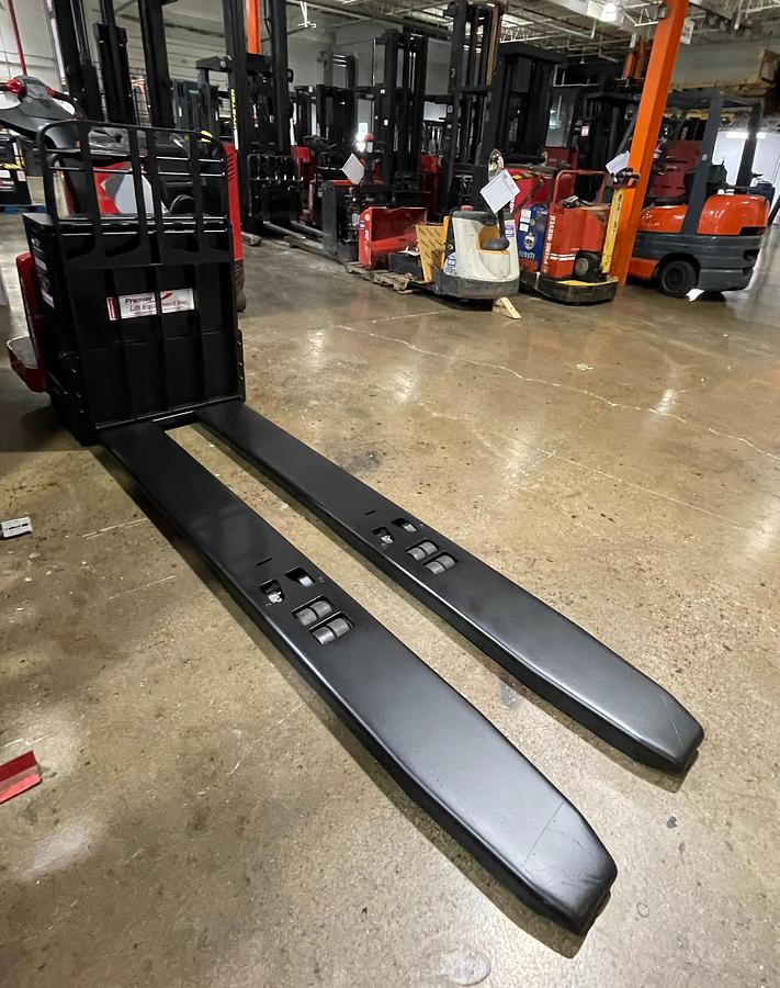 Angled front view of 2015 Raymond 8410 electric rider pallet jack – CSA-certified 6,000 lb chassis with tapered long forks, ergonomic tiller, and clean repaint shown staged in Brampton ON – Premier Lift Equipment