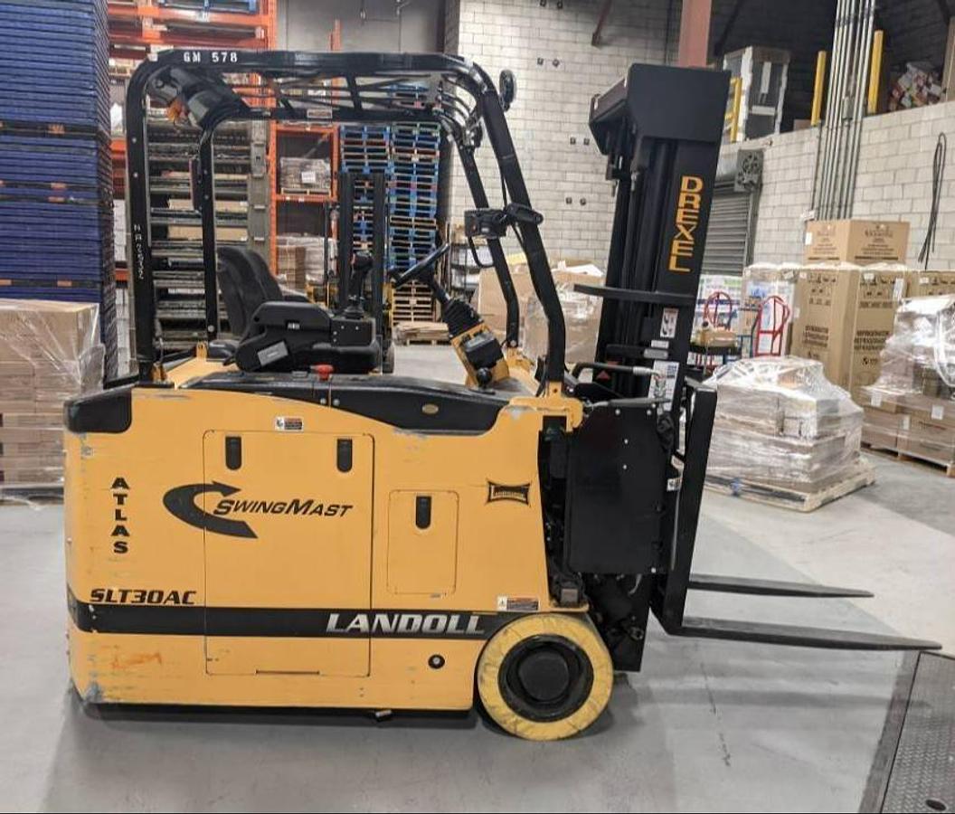 Side profile of 2016 Drexel SLT30AC electric SwingMast forklift showing pivoting mast, directional wheels, and narrow chassis during Brampton deployment
