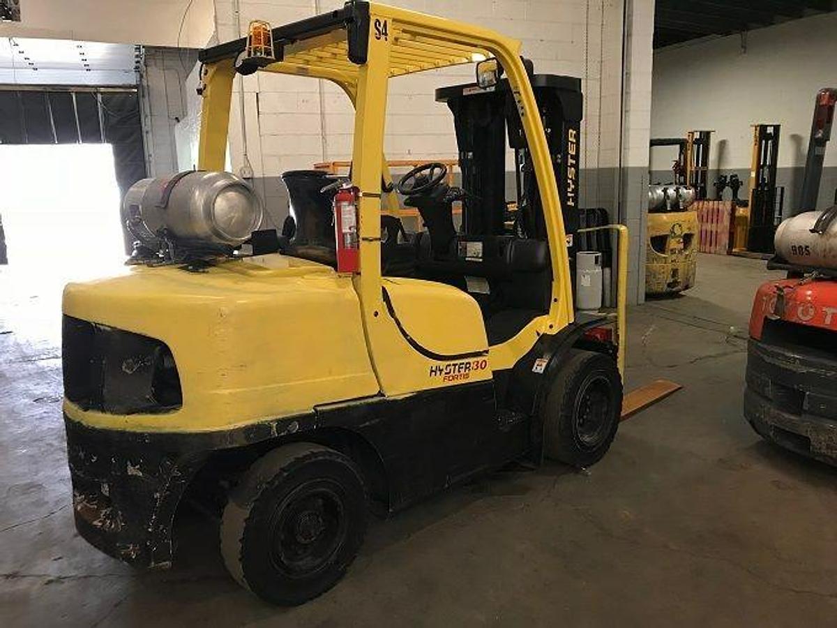 Side view of refurbished 2011 Hyster H80FT LP Gas forklift showing solid pneumatic tires, load backrest, cowling mount, and 3‑stage mast with side shift during Ontario deployment.