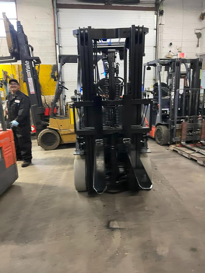 Head-on view of 2019 Toyota 8FBCU25 electric forklift with forks lowered, triple mast extended, and CSA safety markings visible