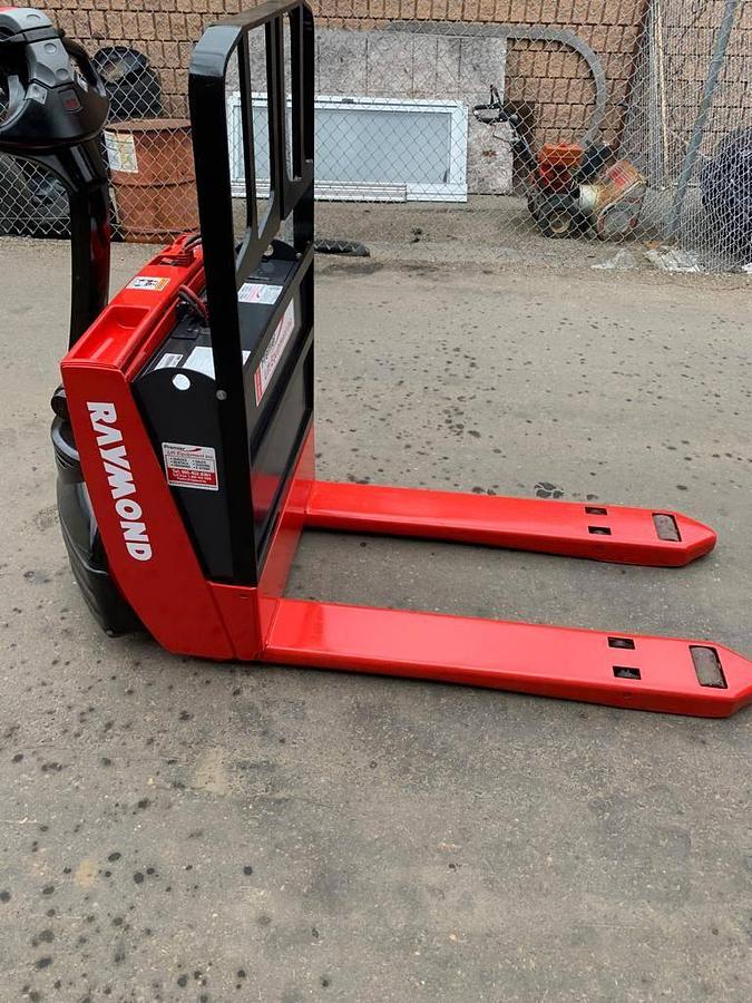 Angled opposite side view of refurbished 2014 Raymond 102T-F45L electric walkie pallet truck showing drive unit cover, tiller arm, and fork tips during Oakville deployment