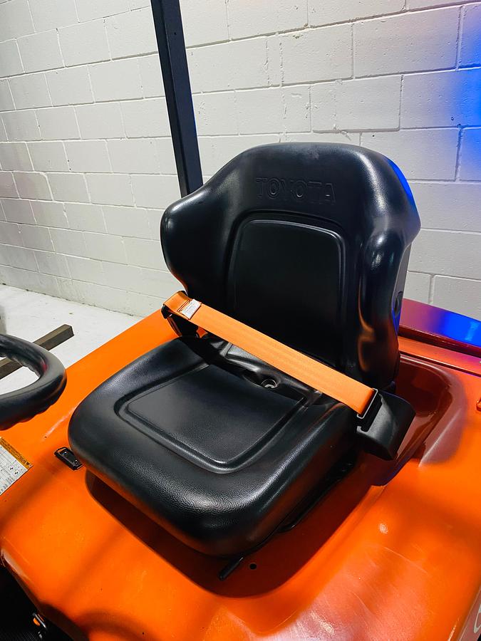 Operator seat on 2015 Toyota 7FBEU15 electric forklift showing orange retractable seat belt, ergonomic cushion seat, and CSA-certified chassis – unit staged in Brampton ON