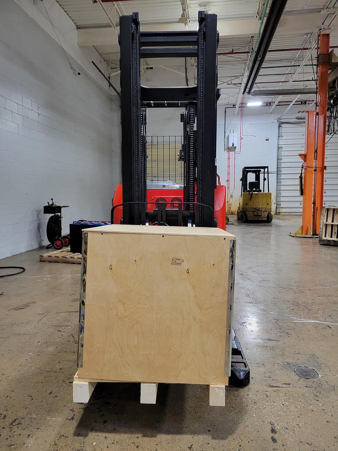 Front angled view showing mast rails, compact chassis profile with battery charger on forks