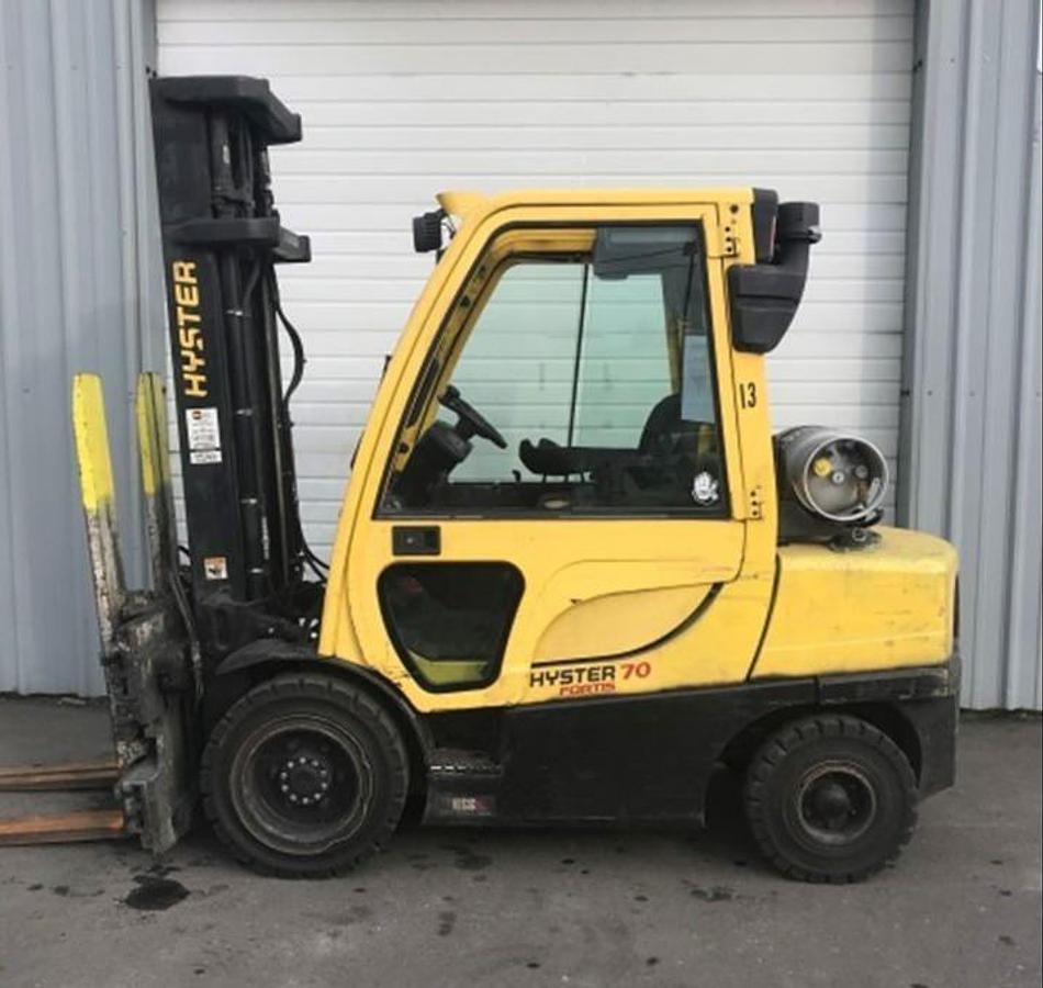 Side view of refurbished 2012 Hyster H70FT LP Gas forklift showing full cab, solid pneumatic tires, 3‑stage mast, and CSA certification decal during Ontario deployment.