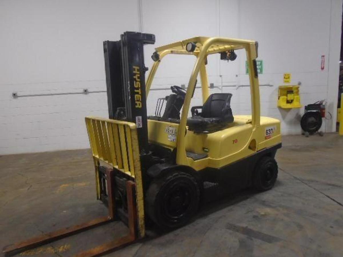 Front side angle of refurbished 2006 Hyster H70FT diesel pneumatic forklift showing 3-stage mast, side shifter, forks, pneumatic tires, and operator cab with CSA safety decals during Brampton deployment