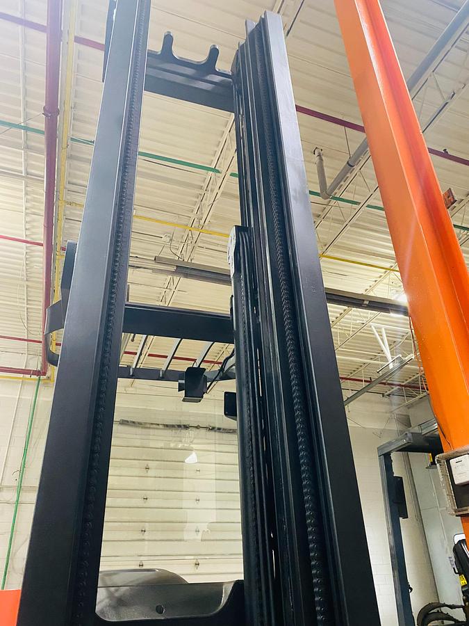 Close‑up of mast channel on Budget Raymond reach truck — rails, rollers, and lift chains visible.